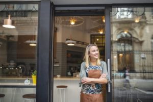 happy small business owner stands in the doorway of her cafe