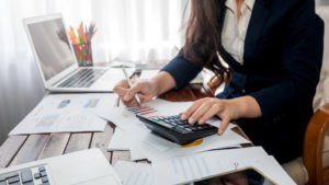 a professional woman uses a calculator on a desk covered with graphs and accounting documents